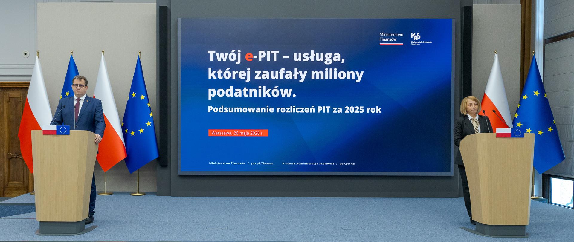 Dwie osoby stoją przy oddzielnych mównicach, a między nimi ekran z napisem „Twój e‑PIT – usługa, której zaufały miliony podatników” oraz informacją o podsumowaniu PIT za 2025 rok.