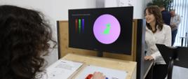 Dziewczynka siedzi przed monitorem, na nim obrazek zielonego kota na różowym tle.
