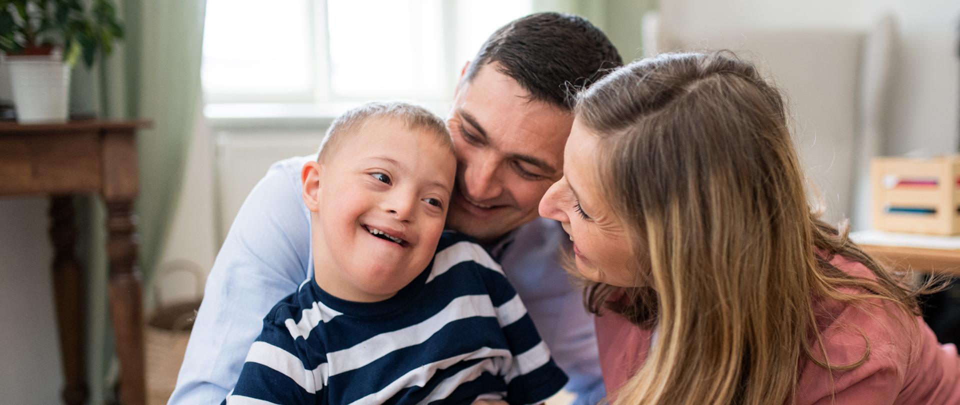 A cheerful down syndrome boy with parents indoors at home hugging.
