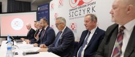 Minister Grzegorz Puda siedzi przy stole i przemawia do mikrofonu, po jego prawej stronie wiceminister pracy i polityki społecznej Stanisław Szwed
