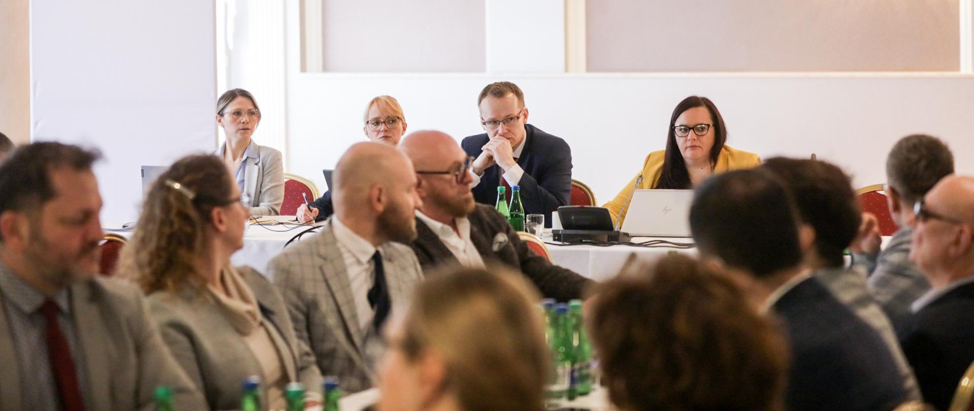 Uczestnicy posiedzenia Rady Dostępności siedzą przy długich stołach