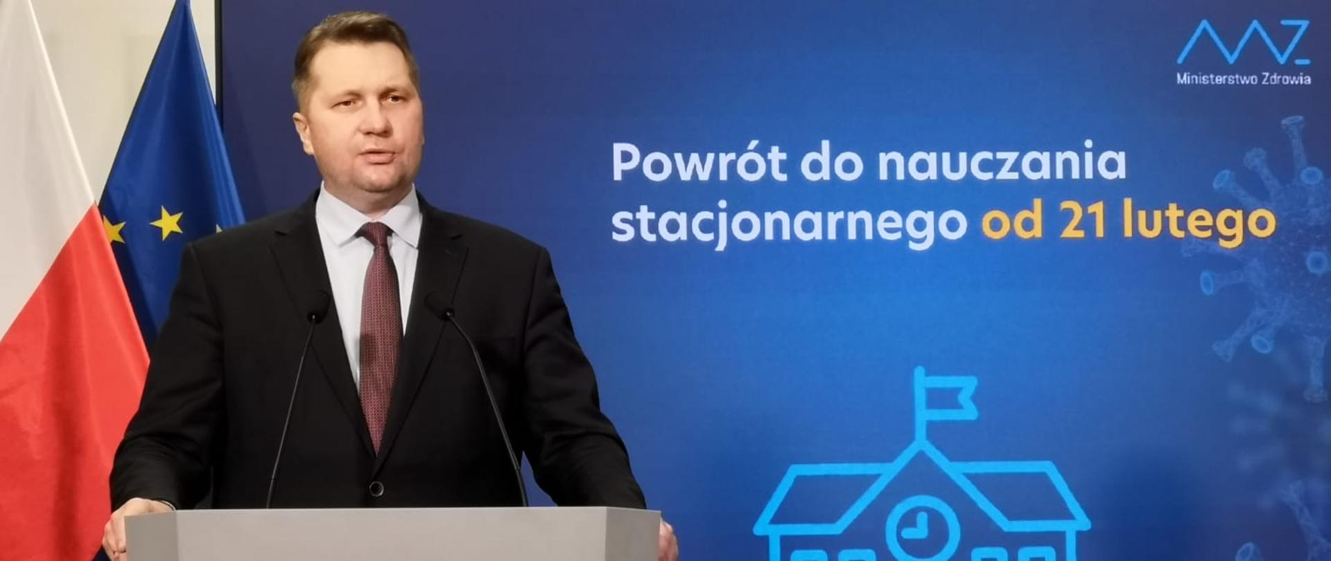  minister czarnek przemawia podczas konferencji przy mównicy z lewej strony, w tle za jego plecami plansza z napisem wracamy do nauki stacjonarnej od 21 lutego