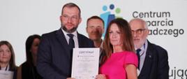 
Minister funduszy i polityki regionalnej Grzegorz Puda wręcza certyfikat uczestnictwa w projekcie Centrum Wsparcia Doradczego Plus, minister trzyma w rękach certyfikat wraz z jedną z uczestników projektu