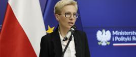 Wiceprezes Łódzkiej Specjalnej Strefy Ekonomicznej Agnieszka Sygitowicz stoi przy mikrofonie i przemawia, za jej plecami baner MFiPR i flagi Polski i UE