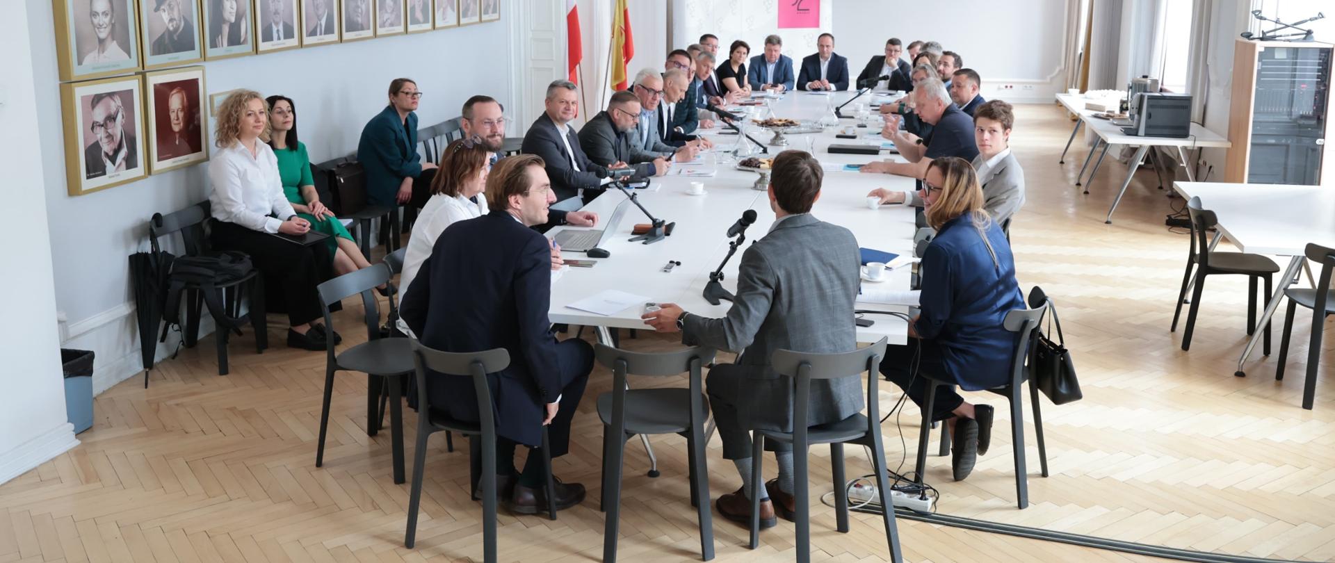 W sali konferencyjnej grupa osób siedzi przy stole.