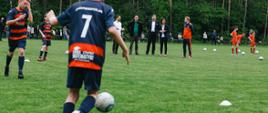 Chłopiec biegnący za piłką na boisku w koszulce z numerem 7. W tle Minister Sportu i Premier.