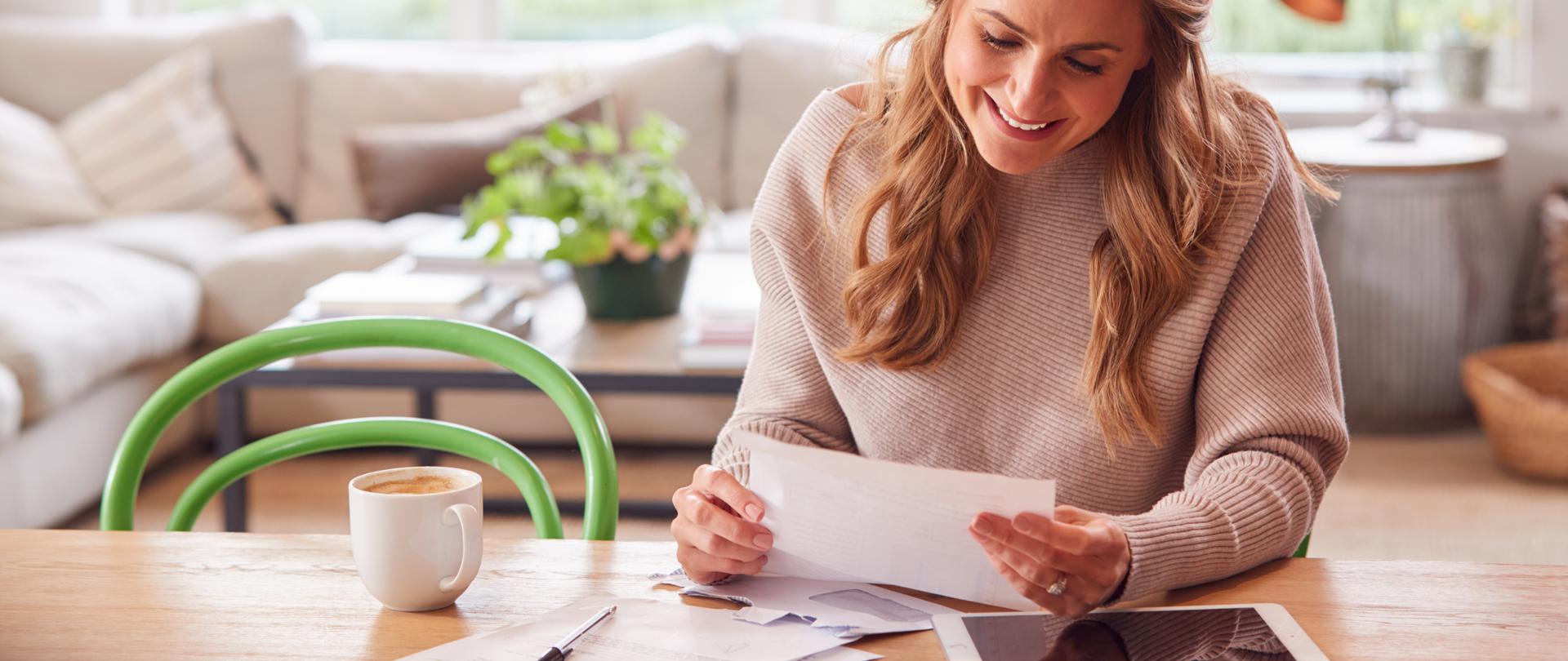 Woman With Digital Tablet Sitting At Table At Home Reviewing Domestic Finances