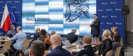 Na zdjęciu widać salę konferencyjną wypełnioną siedzącymi przy stołach uczestnikami spotkania.
