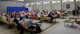 Grupa osób siedzi na sali przy stołach.