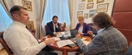 Przy okrągłym stoliku siedzi minister Czarnek i trzy osoby, przed nimi dokumenty i otwarty laptop.
