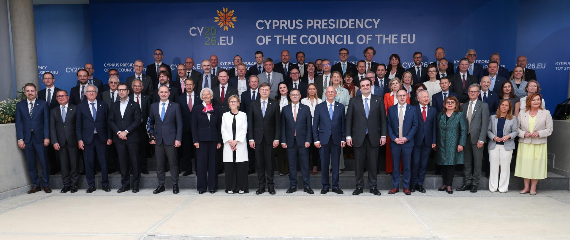 Grupowe zdjęcie uczestników nieformalnego posiedzenia Rady ECOFIN w Nikozji, stojących na schodach przed niebieskim tłem z napisem „Cyprus Presidency of the Council of the EU” i logo CY2026.EU.