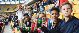 Widok z boku na trybunę stadionu, na żółtych krzesełkach siedzą uczniowie.