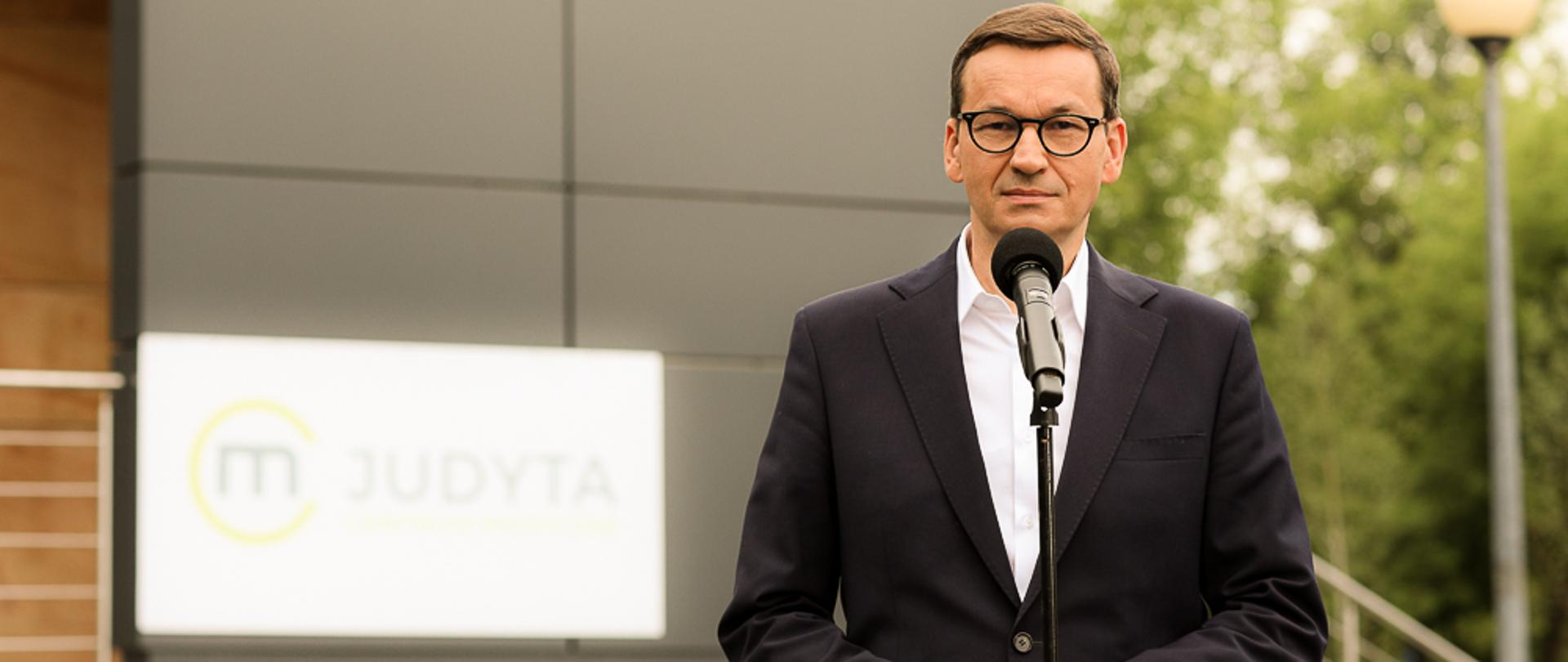 Premier Mateusz Morawiecki stoi podczas konferencji prasowej.