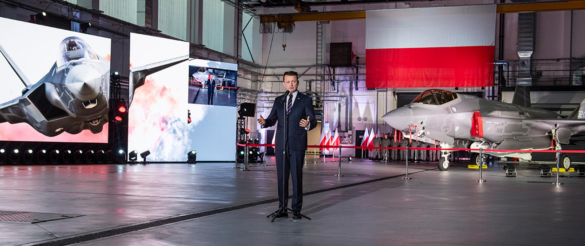 Minister M.Błaszczak przemawia w Dęblinie po podpisaniu umowy na F-35. W tle samolot F-35.