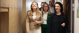 
Minister funduszy i polityki regionalnej Katarzyna Pełczyńska-Nałęcz idzie korytarzem w Branżowym Centrum Umiejętności (BCU) Przemysłu Drzewnego w Kaliszu, obok niej stoją osoby, z którymi zwiedza BCU
