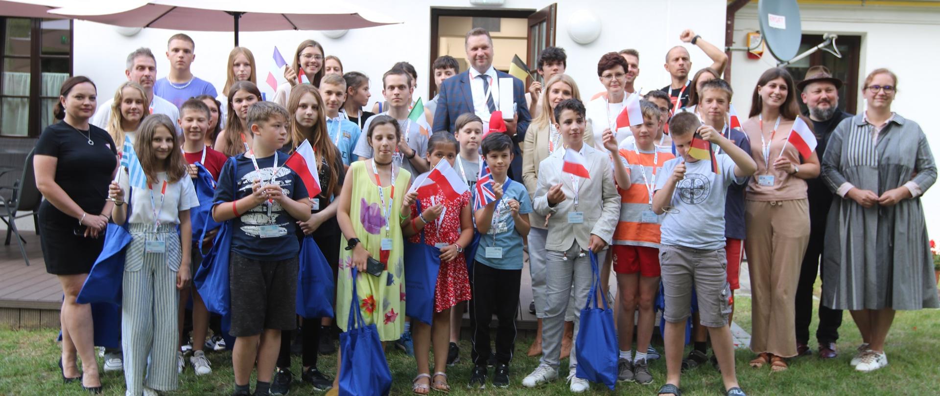 Zdjęcie zbiorowe dużej grupy ludzi stojących na trawie przed starym budynkiem.