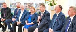 Na ustawionych w rzędzie krzesłach siedzi siedem osób, pośrodku minister Czarnek mówi do trzymanego w ręku bezprzewodowego mikrofonu, w tle żółta ściana na której wiszą korkowe tablice z przypiętymi kolorowymi kartkami.