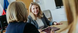 Spotkanie wiceministry funduszy i polityki regionalnej Moniki Sikora z dyrektor Katariną Ivanković Knežević z Dyrekcji Generalnej ds. Zatrudnienia, Spraw Społecznych i Włączenia Społecznego Komisji Europejskiej, ministra Sikora siedzi przy stole i uśmiecha się