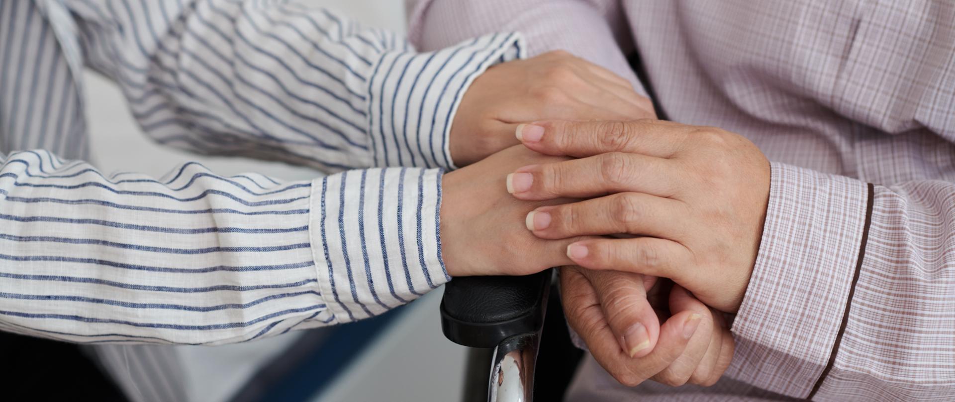 Woman sitting in wheelchair touching hands of daughter visiting her in nursing home