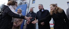Pięć osób stoi przed domem i wita się z młodą dziewczyną.
