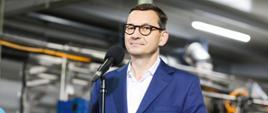 Premier stoi podczas konferencji prasowej w firmie.
