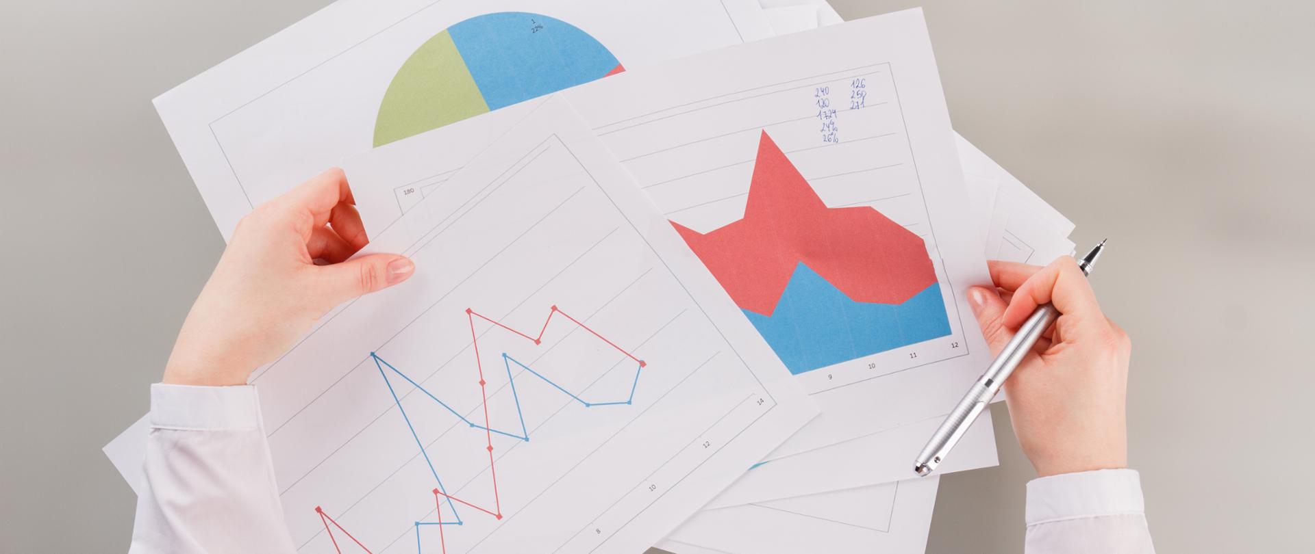 Female hands holding financial documents on table at the office. Statistics data of company.