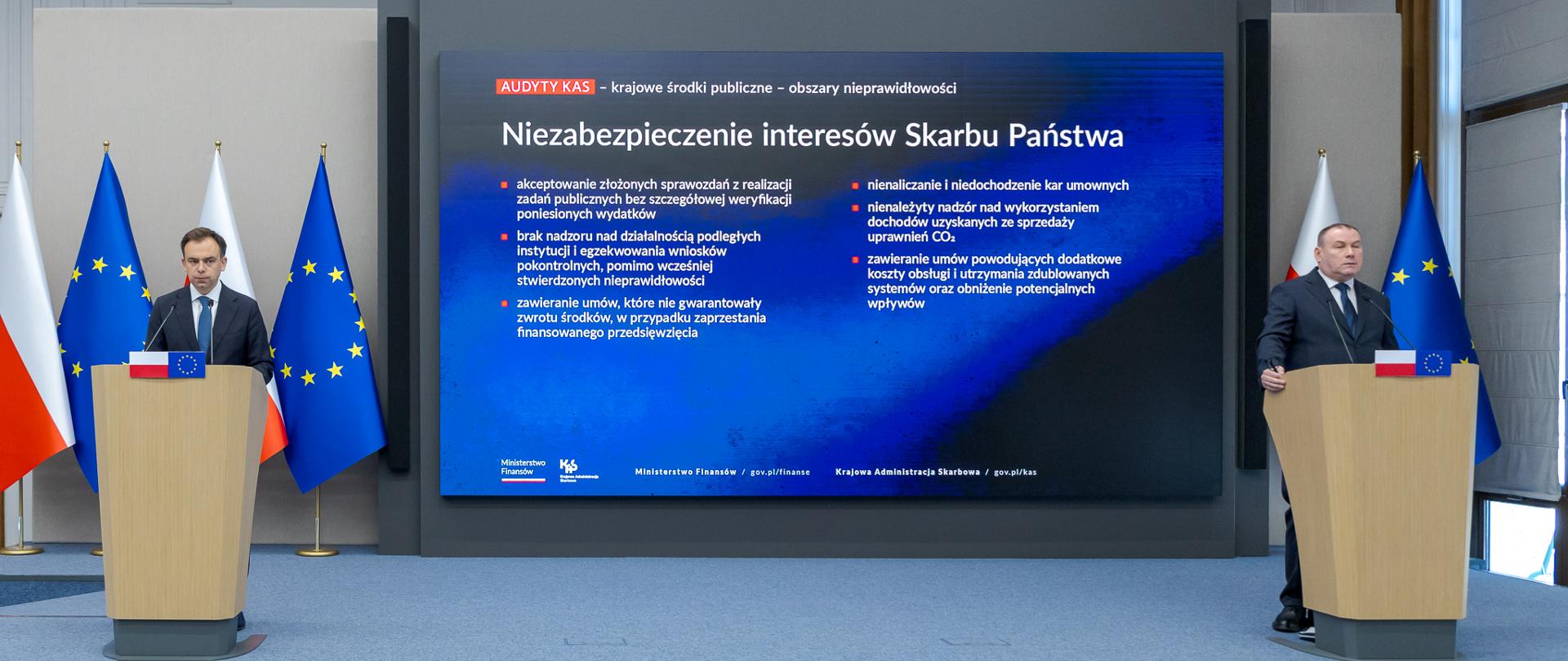 Minister Finansów i Gospodarki Andrzej Domański i Podsekretarz Stanu, Zastępca Szefa KAS Zbigniew Stawicki stoją przy mównicach podczas konferencji poświęconej audytom gospodarowania środkami publicznymi. Na ekranie wyświetlono informacje o stwierdzonych nieprawidłowościach.