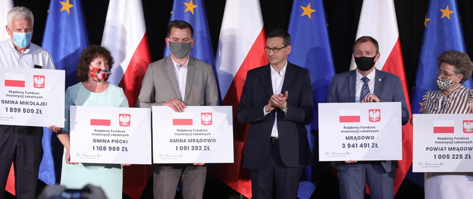 Premier stoi wśród samorządowców, którzy trzymają czeki.