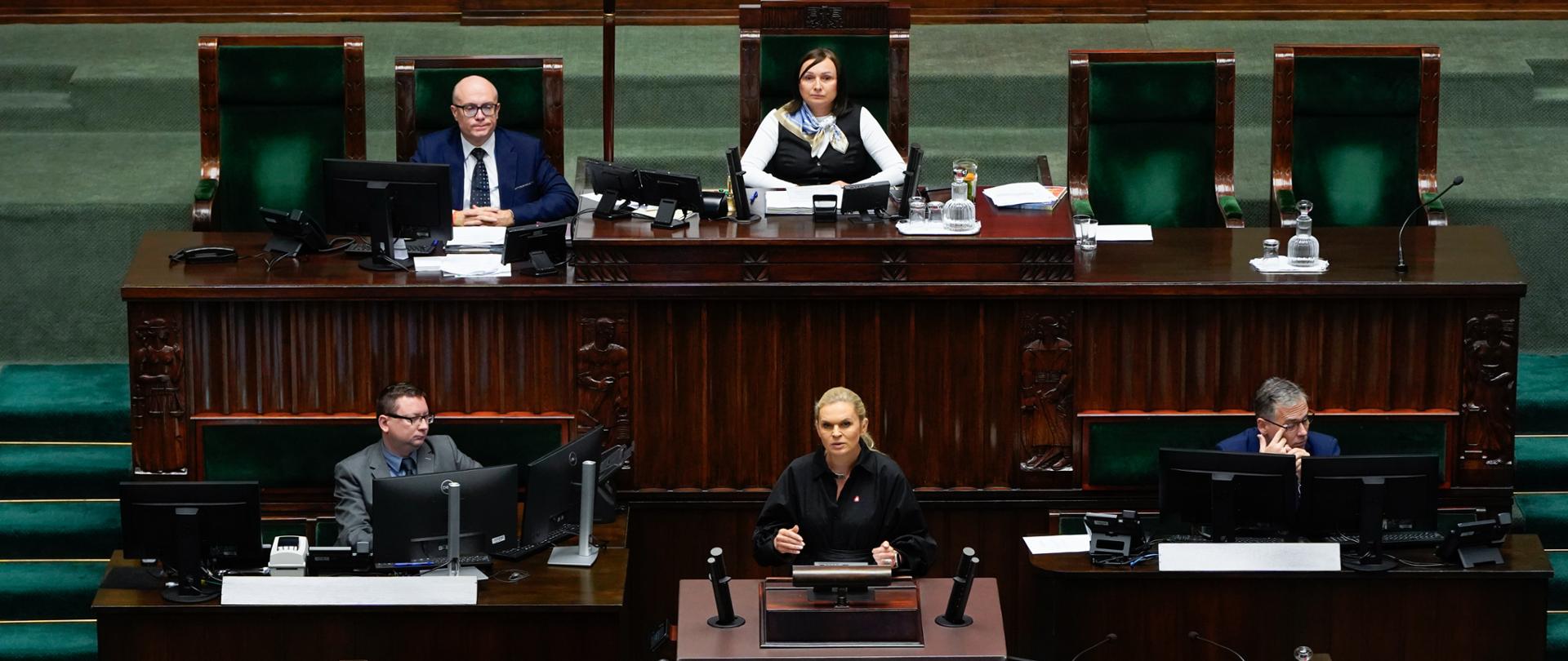 zdjęcie przedstawia Minister Edukacji przy mównicy oraz wicemarszałek sejmu i protokolantów