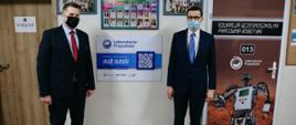 Premier Mateusz Morawiecki i minister Przemysław Czarnek pozują do zdjęcia przy pracowni robotyki w Zespole Szkół w Nowej Sarzynie. Za nimi znajdują się drzwi do pracowni.
