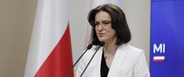 Dyrektor Centrum Unijnych Projektów Transportowych Joanna Lech, pani dyrektor stoi przy mikrofonach i przemawia, za jej plecami flagi Polski 