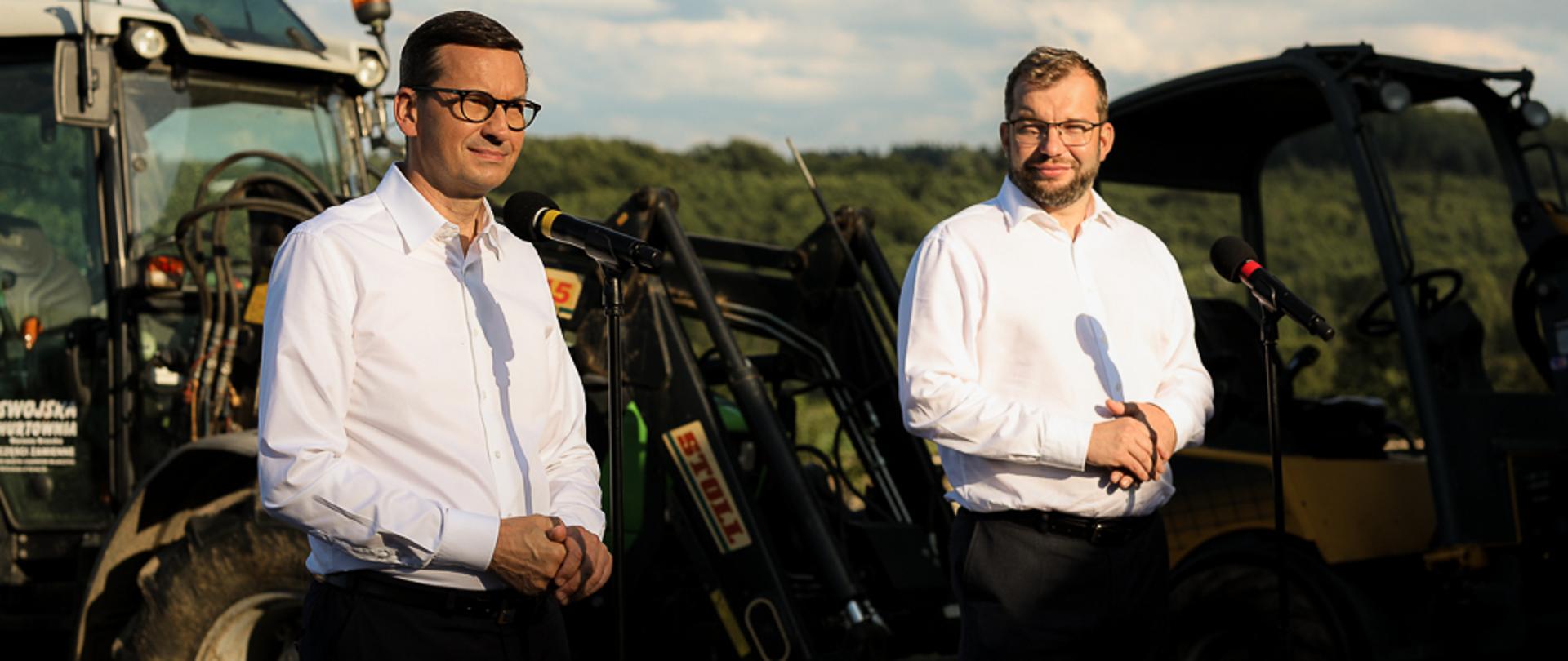 Premier Mateusz Morawiecki wraz z Ministrem Rozwoju Rolnictwa i Wsi podczas konferencji, w tle maszyna rolnicza traktor.