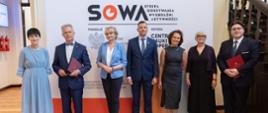 Uczestnicy uroczystości stoją na tle ścianki z napisem SOWA, obok korytarz i schody. fot. P.F. MATYSIAK