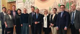 Ludzie pozujący do zdjęcia (m.in. wiceminister edukacji narodowej – Maciej Kopeć ) na tle ściany z namalowaną panoramą Wilna.