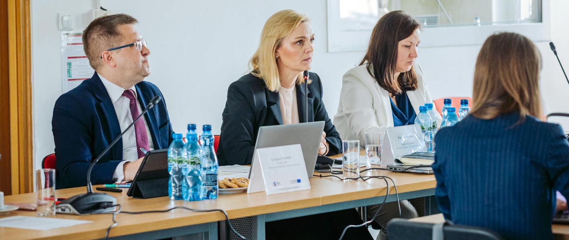 Trzy osoby siedzą obok siebie przy stole.