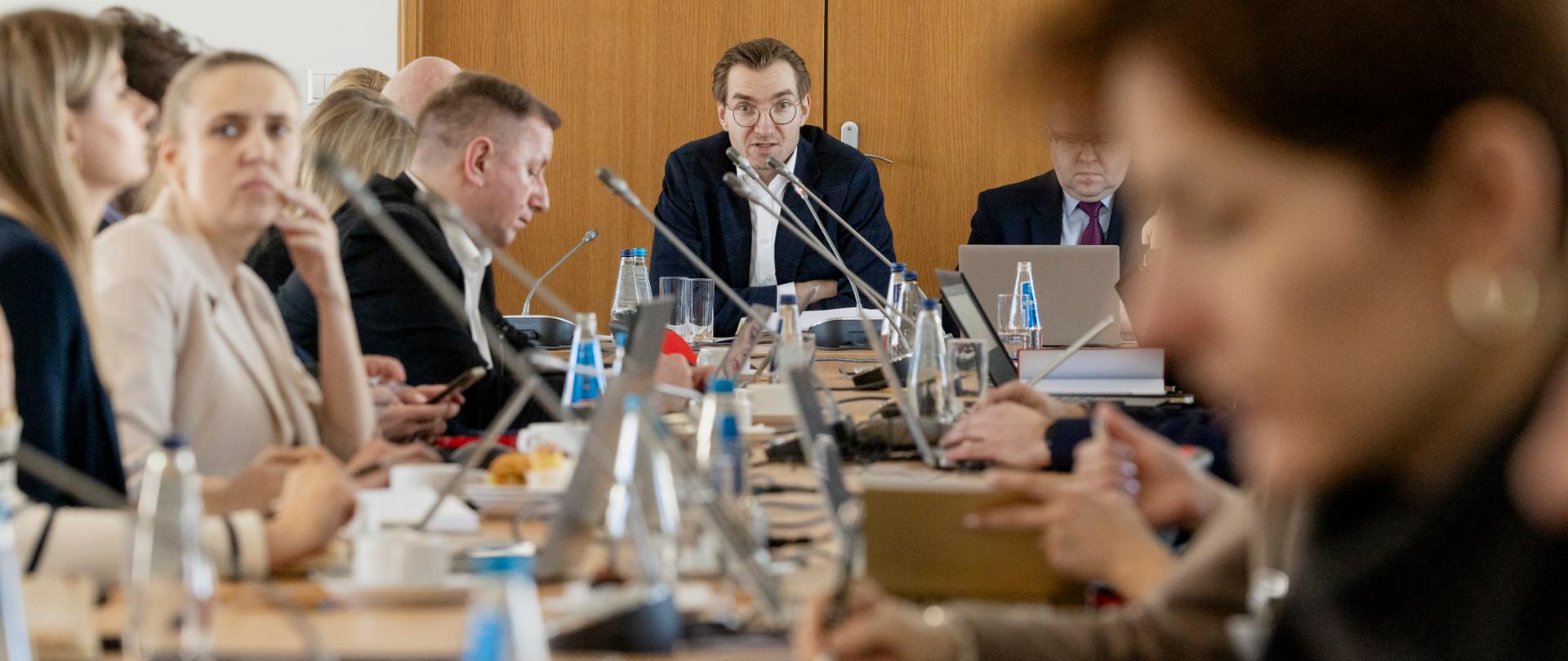 W sali konferencyjnej grupa osób siedzi przy stołach. Na pierwszym planie wiceminister Jan Szyszko.