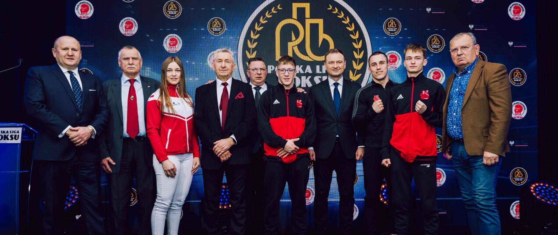 Minister sportu i turystyki, prezes PZB oraz zawodnicy stoją na tle ekranu z logiem Polskiej Ligi Boksu