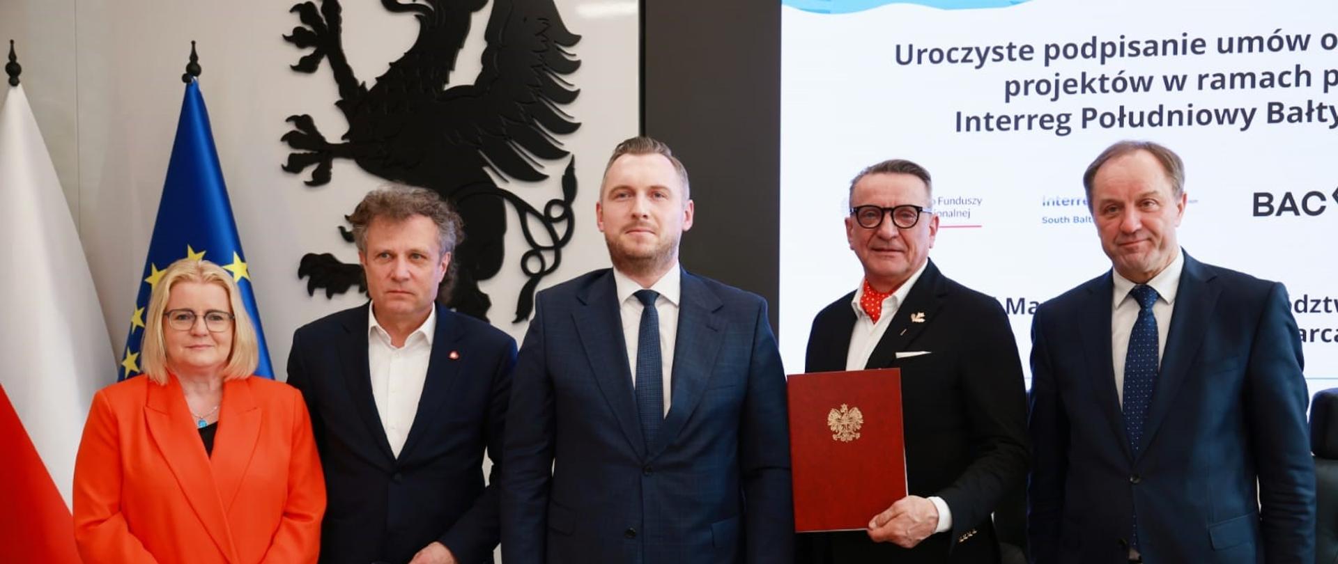 Pięć osób stoi obok siebie za stołem. Wśród nich jako drugi i trzeci od lewej wiceministrowie Jacek Karnowski i Konrad Wojnarowski. 
