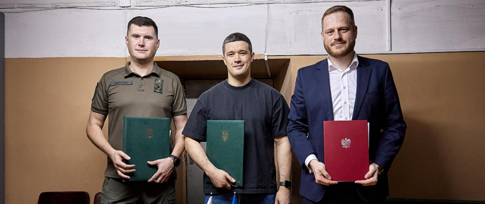Zdjęcie ministra Janusza Cieszyńskiego i wicepremiera Mychajło Fedorowa. Panowie trzymają w rękach teczki - odpowiednio czerwoną z polskim orzełkiem i zieloną z godłem Ukrainy. 