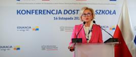 Wiceminister Machałek stoi przy mównicy i mówi do mikrofonu, za nią na ścianie napis Konferencja dostępna szkoła - 16 listopada 2022 r.
