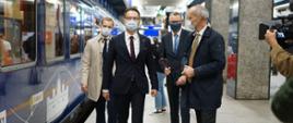 Wiceminister Waldemar Buda peronem przechodzi obok pociągu Connecting Europe Express, dziennikarze aparatami robią zdjęcia i kamerami filmują to przejście