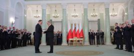 Prezydent Andrzej Duda wręcza nominację Jerzemu Kwiecińskiemu na ministra finansów, inwestycji i rozwoju, w tle członkowie rządu, zebrani goście i polskie flagi