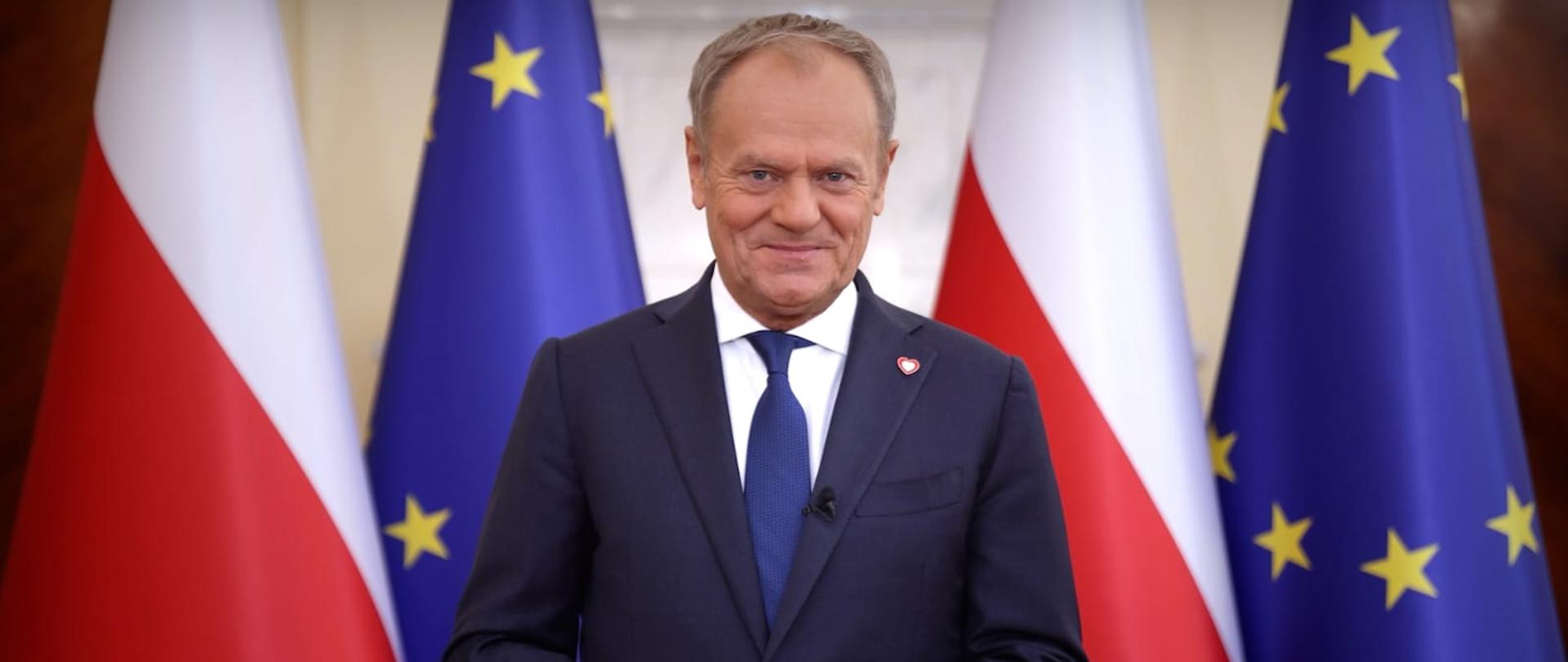 Premier Donald Tusk podczas orędzia 1 maja 2025 r. W tle flagi Polski i UE.