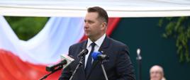 Minister mówi do mikrofonów, za nim polska flaga.