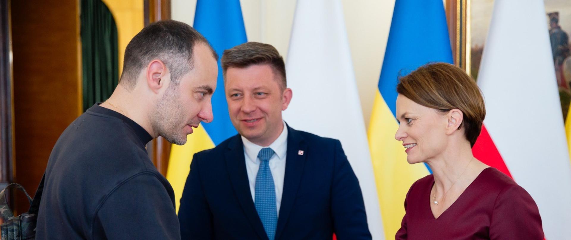 Trzy osoby rozmawiają ze sobą i ściskają sobie dłonie.