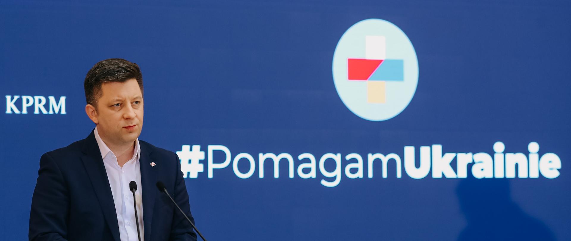 Szef KPRM na tle napisu #PomagamUkrainie.