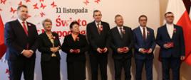 Zdjęcie zbiorowe, pod ścianą z napisem 11 listopada święto niepodległości stoi minister Czarnek i kilka elegancko ubranych osób.