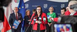 Na pierwszym planie Sekretarz Stanu Małgorzata Jarosińska-Jedynak w czasie konferencji prasowej. Widać również 8 innych osób. 