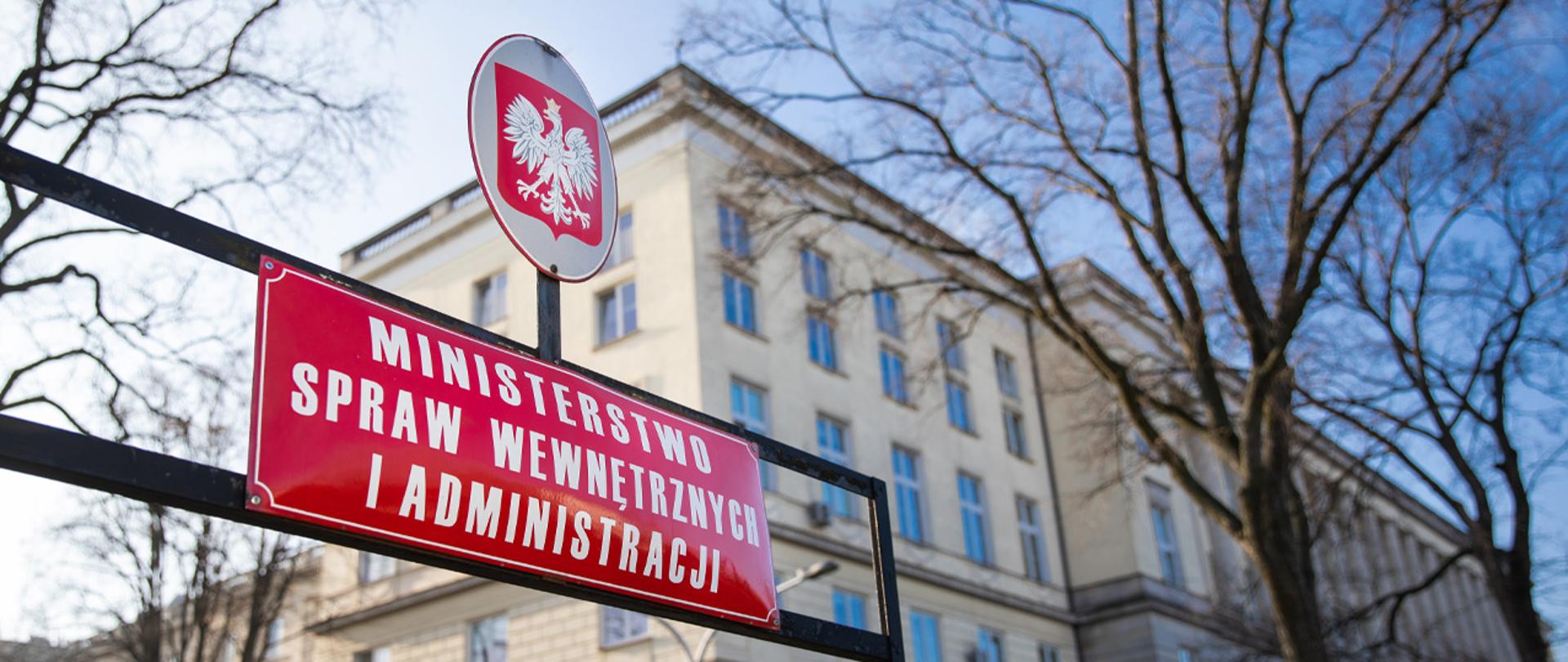 Tabliczki z orłem w koronie i napisem " Ministerstwo Spraw Wewnętrznych i Administracji", w tle budynek MSWiA.