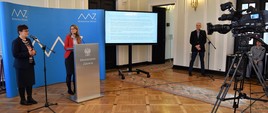 Konferencja prasowa w Ministerstwie Zdrowia. Na zdjęciu podsekretarz stanu Katarzyna Głowala oraz prof. dr hab. Magdalena Durlik z Kliniki Medycyny Transplantacyjnej i Nefrologii WUM na tle niebieskiej ścianki Ministerstwa Zdrowia. Naprzeciwko nich ustawiona kamera.